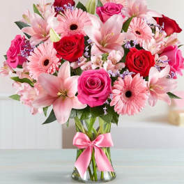 Pink and red bouquet of roses, lilies, and gerbera daisies in a glass vase