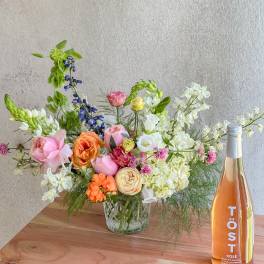 Mixed bouquet in a glass vase beside a bottle of rosé sparkling drink