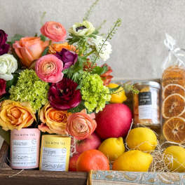 Mixed bouquet with citrus and tea gift items in a wooden crate