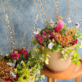 Two mixed floral arrangements in ribbed beige pots with tall curly branches