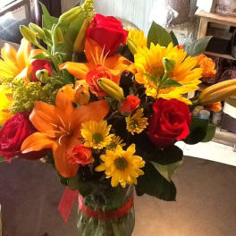 Bouquet of red roses, orange lilies, and yellow daisies in a glass vase
