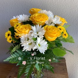 Arrangement of yellow roses and white daisies in a clear glass vase on a wooden surface