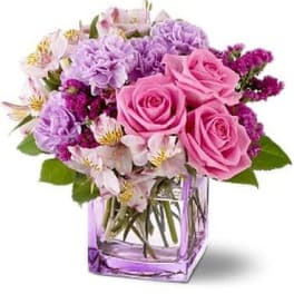 Compact bouquet of pink roses and purple flowers in a lavender glass cube vase