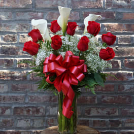 Red roses and white calla lilies in a glass vase with a red ribbon