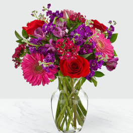 Bouquet of red roses, pink gerbera daisies, and purple flowers in a glass vase