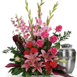 Pink lilies and roses arranged beside a silver urn.