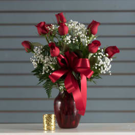 Arrangement of red roses with white filler flowers in a red vase with a large red bow.