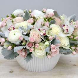 Low pastel arrangement of white and blush roses, ranunculus, and orchids in a white ceramic bowl
