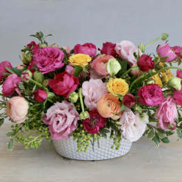 Low centerpiece of bright pink, yellow, and peach blooms in a white textured ceramic bowl