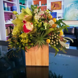Mixed floral arrangement in a wooden cube vase with green and yellow blooms