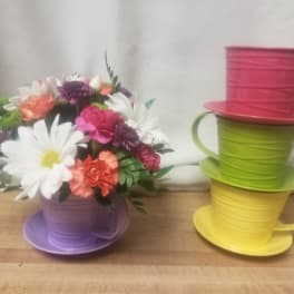 Colorful bouquet in a purple teacup-shaped container beside stacked teacup planters