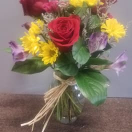 Bouquet of red roses, yellow daisies, and purple flowers in a glass vase