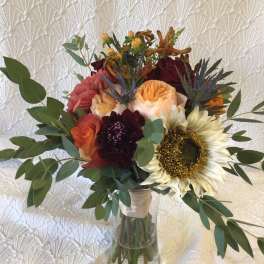 Mixed bouquet with a sunflower, roses, and dark blooms in a glass vase