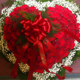 Heart-shaped arrangement of red roses with white baby's breath and a red ribbon bow