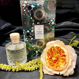 Perfume bottle, floral candle box, and a peach rose on dark fabric