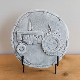 Round gray decorative plaque with a tractor relief on a stand