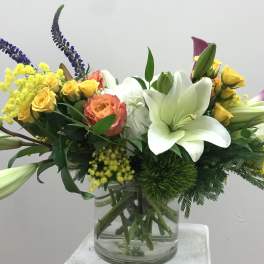 Mixed bouquet with white lilies, yellow roses, and purple spikes in a glass vase