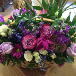 Basket arrangement of pink, purple, and white flowers with glossy greenery