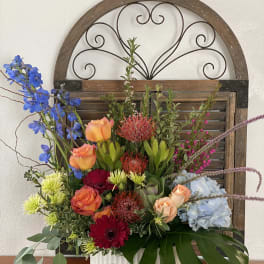 Mixed floral arrangement in a white vase with blue, orange, red, and pale blue blooms