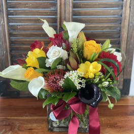 Mixed bouquet in a glass vase with white calla lilies, roses, and bright yellow blooms
