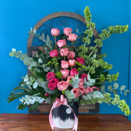 Pink rose arrangement in a white vase with a pink ribbon