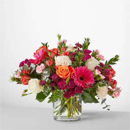 Mixed bouquet of pink, white, and orange flowers in a clear glass vase