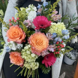 Handheld bouquet with orange roses, pink gerberas, and blue flowers