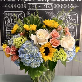 Mixed bouquet of sunflowers, roses, and hydrangeas in a glass vase
