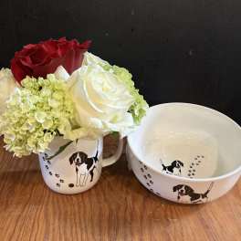 Small bouquet of red, white, and pale green flowers in a dog-print mug beside a matching bowl