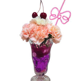 Pink carnations in a purple glass vase with cherries and a bow-shaped stirrer