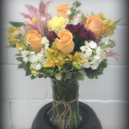 Mixed bouquet of peach roses, pink lilies, and white blooms in a glass vase