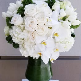 White rose and orchid bouquet in a green glass vase