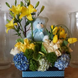 Yellow lilies and roses arranged with a blue teddy bear in a box