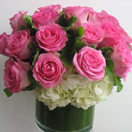 Pink roses arranged above white hydrangeas in a green vase