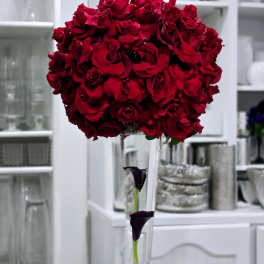 Tall bouquet of red roses in a clear vase with dark calla lilies