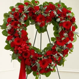 Heart-shaped red floral wreath on a stand with a red ribbon