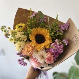 Hand-tied bouquet with a sunflower, roses, and pastel blooms in brown paper