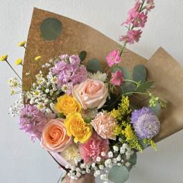 Hand-tied bouquet of pink, peach, and yellow flowers wrapped in brown paper