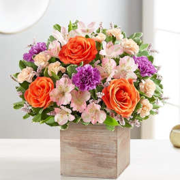 Bouquet of orange roses, pink alstroemeria, and purple carnations in a wooden box