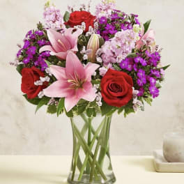 Bouquet of pink lilies and red roses in a clear glass vase