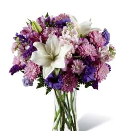 Purple and pink mixed bouquet with white lilies in a clear glass vase