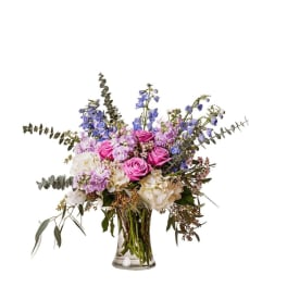 Bouquet of pink roses, blue delphinium, and white hydrangeas in a glass vase