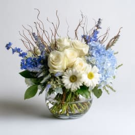 White roses and blue flowers arranged in a clear glass bowl vase.