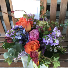 Mixed bouquet with orange and purple roses in a white container
