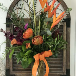 Tropical bouquet with orange bird-of-paradise and orange pincushion blooms in a glass vase