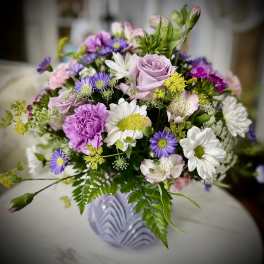 Mixed bouquet of pink, purple, and white flowers in a lavender vase