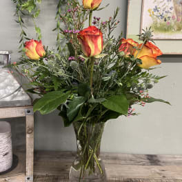 Orange-yellow roses in a clear glass vase with mixed greenery