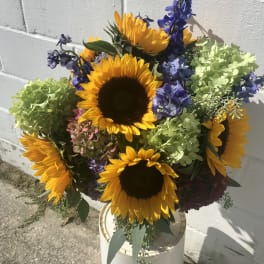 Bouquet of sunflowers and blue-purple flowers in a white container