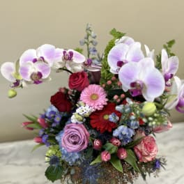 Mixed bouquet with orchids, roses, gerbera daisies, and tulips in a glass vase