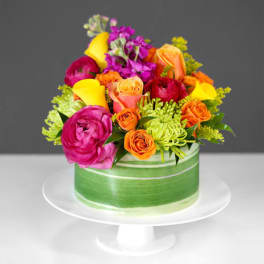 Bright mixed bouquet in a green ribbon-wrapped round box on a white stand